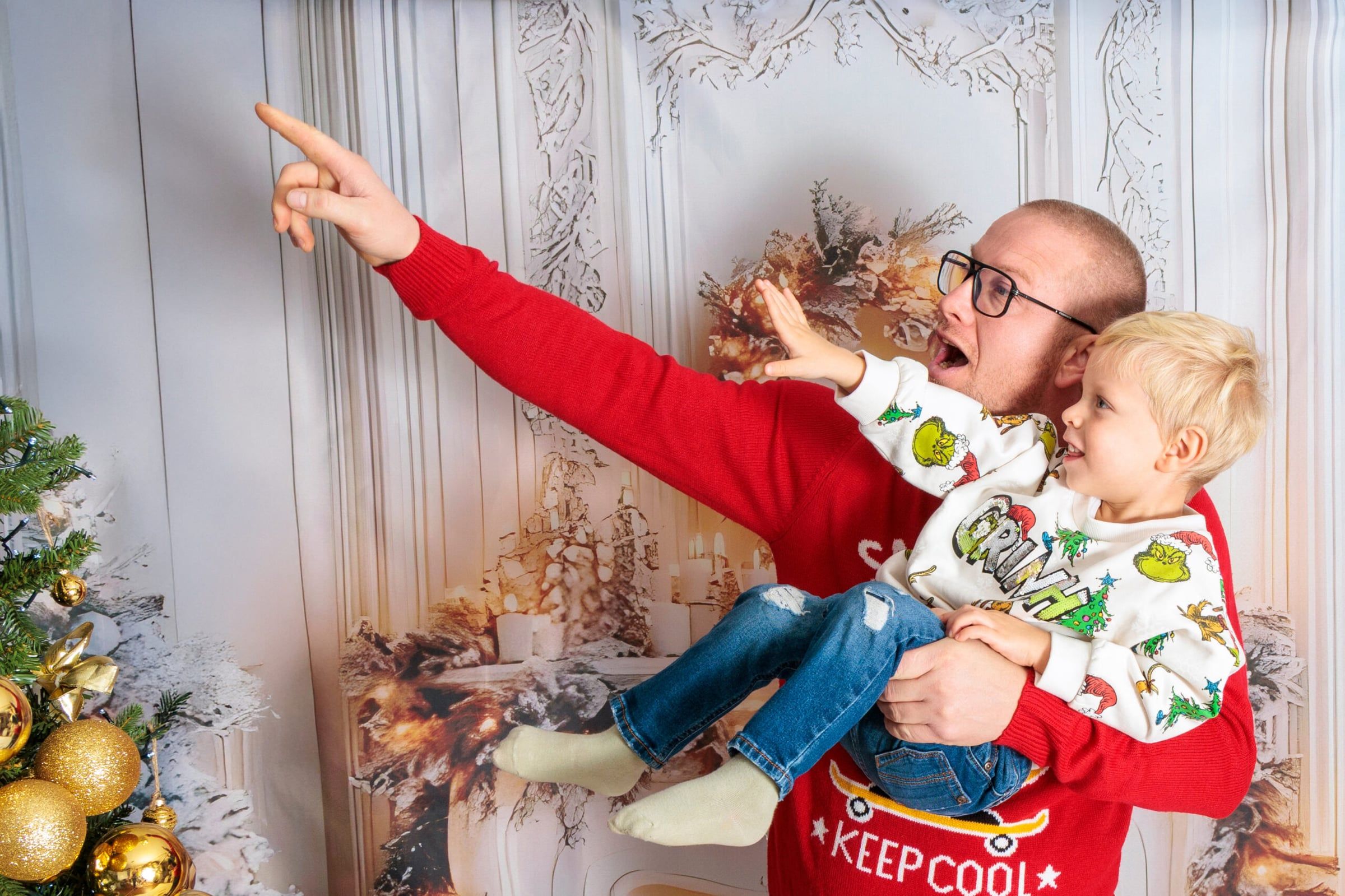 Apa a kisfiát tartja és felfelé mutat, karácsonyi díszletben