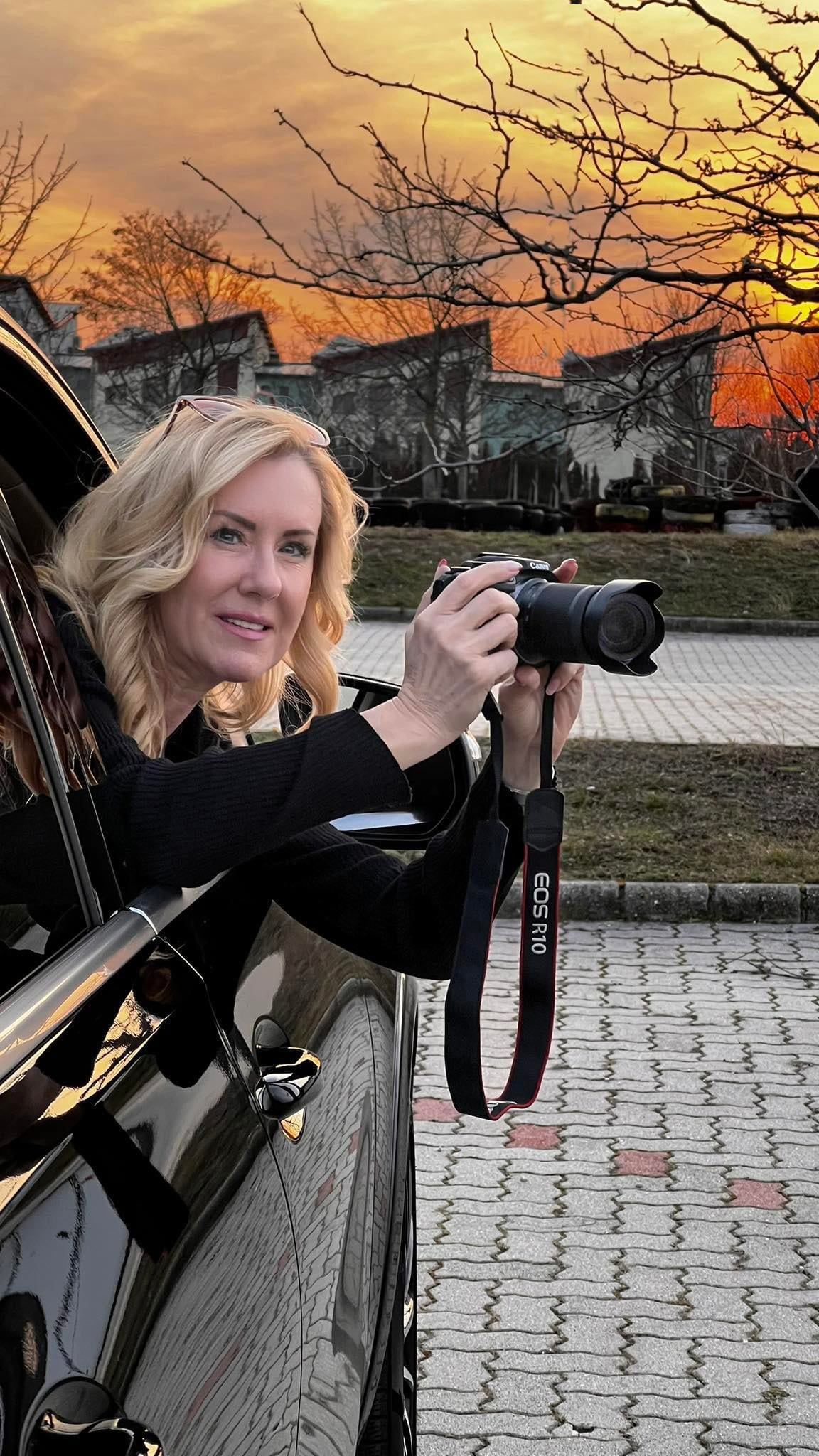 Gyarmati Gabriella fényképezőgéppel egy autó ablakából hajol ki naplementében
